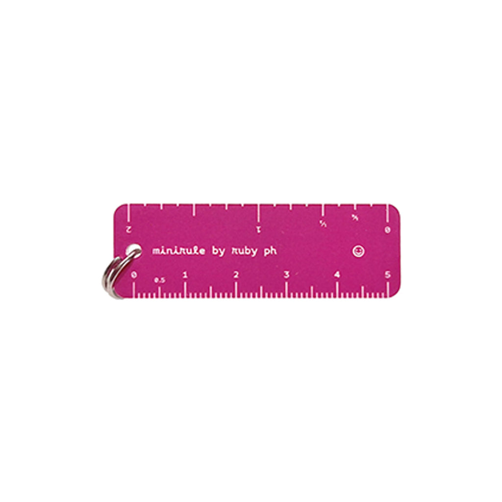 A pink metal pocket ruler with white markings and a silver split ring, featuring the text 'minirule by ruby ph' on a plain white background.