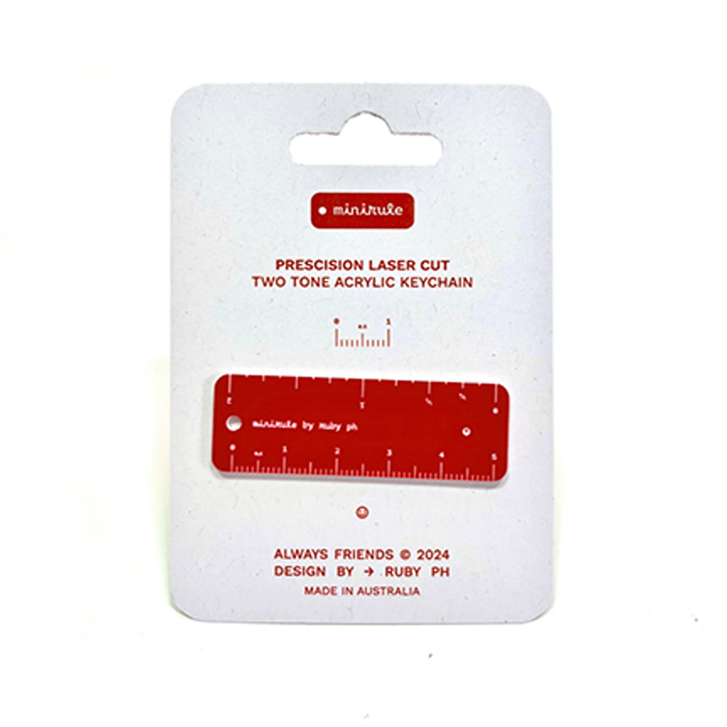 A two-tone acrylic ruler shown on its white retail card. The keychain itself is red, while the backing card is white with red printed text and branding.