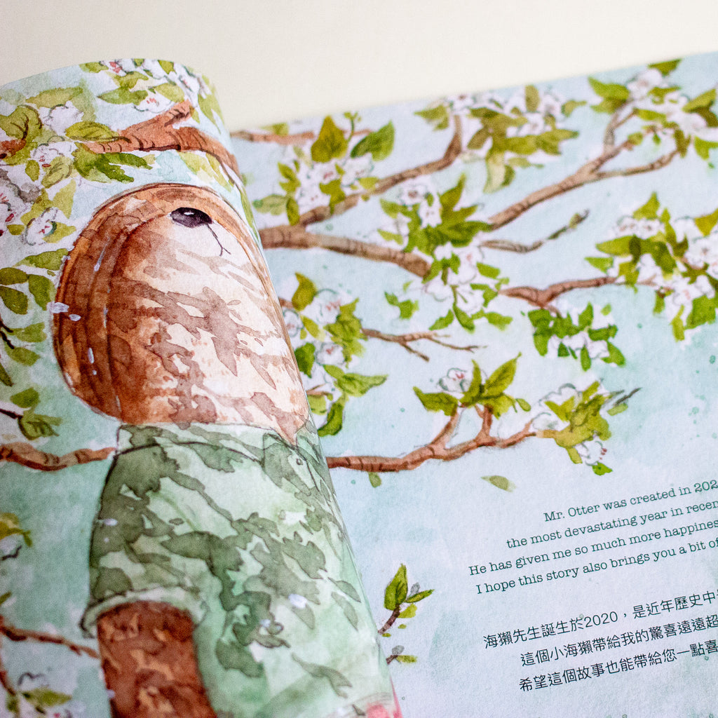 An open illustrated book showing a watercolour-style scene with a brown otter wearing a green shirt among leafy branches, with printed text on the right page.