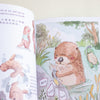 An open children's book showing a watercolour-style illustration of an otter in shallow water, with partial text and additional illustrated figures on the left page.
