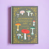 Book titled 'Mushroom Botanical Art' with illustrations of mushrooms on a purple background