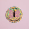 A round glitter sticker featuring a pink butterfly with a black body and the text 'my life is in perfect flow' on a light pink background.