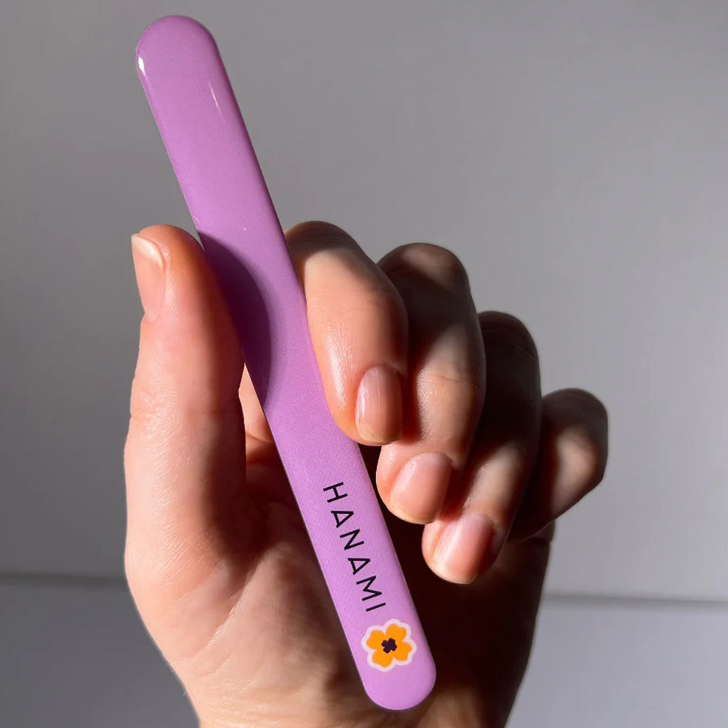 Hand holding a lilac nail file with 'HANAMI' branding against a neutral background