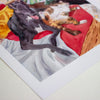 Print of a dog and cat lying on a red blanket with a wicker basket.