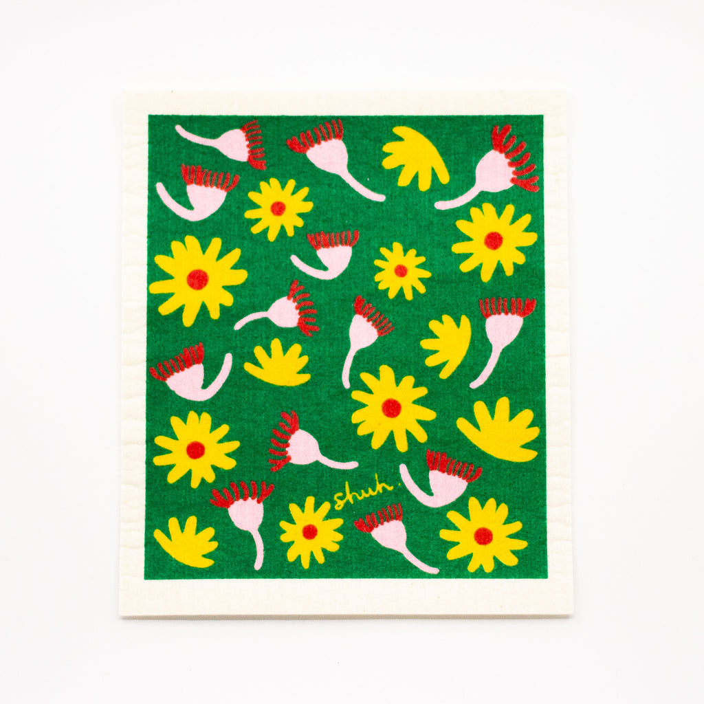 A top view of the shuh and spruce native flora dish cloth. Yellow and pink flowers on a green background. 