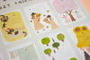 A close-up of a printed calendar page showing several illustrated monthly calendar spreads with whimsical drawings, including a cat, people holding flowers, trees, and sunflower on hat on a pale background.