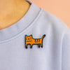 Light blue sweatshirt with an embroidered orange cat design on a peach background