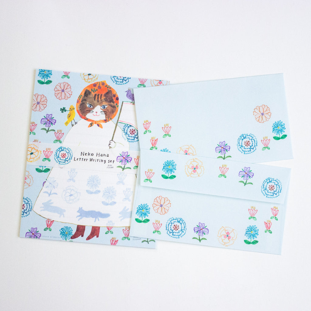 A Neko Hana letter writing set featuring a light blue envelope with a floral pattern, a matching writing sheet of a cat in a dress, all arranged on a white background.