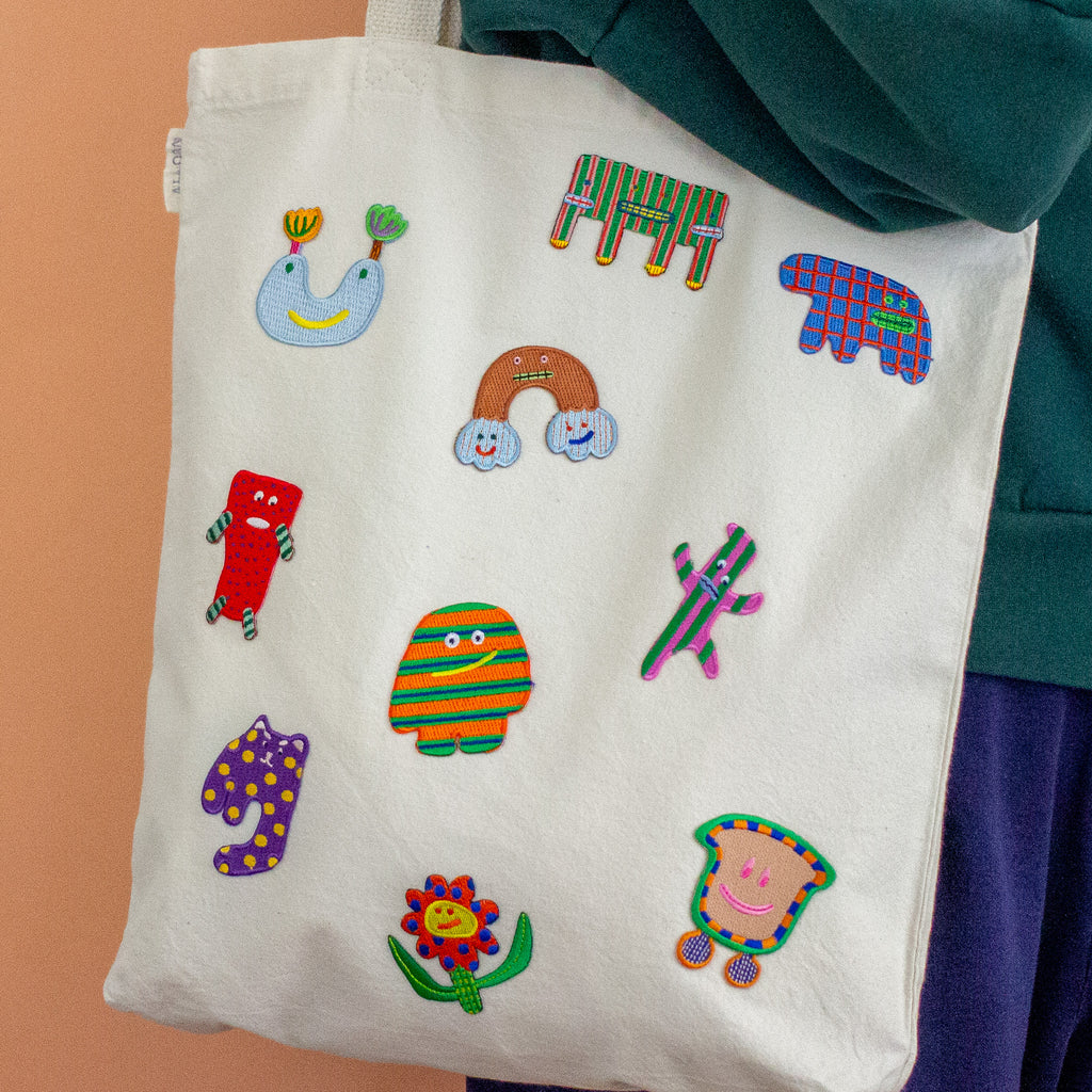 White tote bag with colorful embroidered patches on a peach background