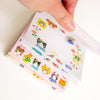 A hand holding a stack of colourful memo pad sheets featuring cute cartoon animal characters and flowers on a white background.