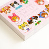 A pink notebook or book cover featuring cute illustrated animals in colourful floral outfits, with the text 'niko niko SMILE!' and 'AIKO FUKAWA' printed on the cover, photographed on a white background.