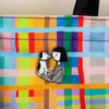 Enamel pin featuring a girl and a dog touching noses, on a colourful bag. 