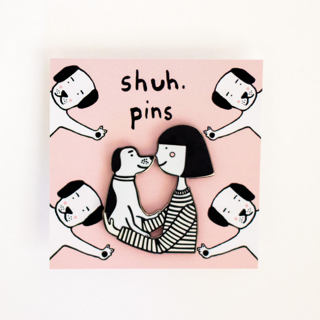 Enamel pin featuring a girl and a dog touching noses. 