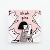 Enamel pin featuring two hand-drawn characters, a girl and her cat, touching noses in a kiss, displayed on a pink card with cat illustrations and the words “shuh. pins”.