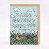 A greeting card with a kraft envelope behind it, featuring a light blue sky, white clouds, and a grassy field with a small illustrated figure. The card reads 'DOING NOTHING WITH YOU MEANS EVERYTHING TO ME'.