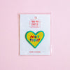 A heart-shaped embroidered patch with the text 'NOT TODAY' in colourful letters, outlined in green, displayed on a white backing card with a clear plastic sleeve against a solid pink background.