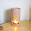 Pink cylindrical oil burner with a smiley face design on a wooden surface.