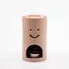 Dusty Pink coloured Ceramic oil burner with smiley face design on a white background