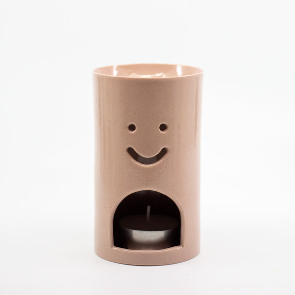 Dusty Pink coloured Ceramic oil burner with smiley face design on a white background