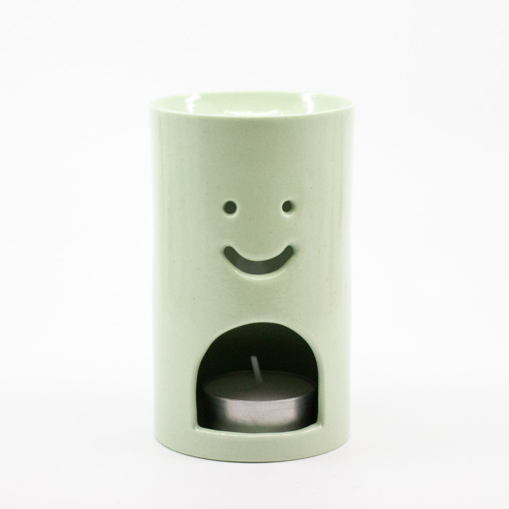 Light green oil burner with a smiley face design on a white background