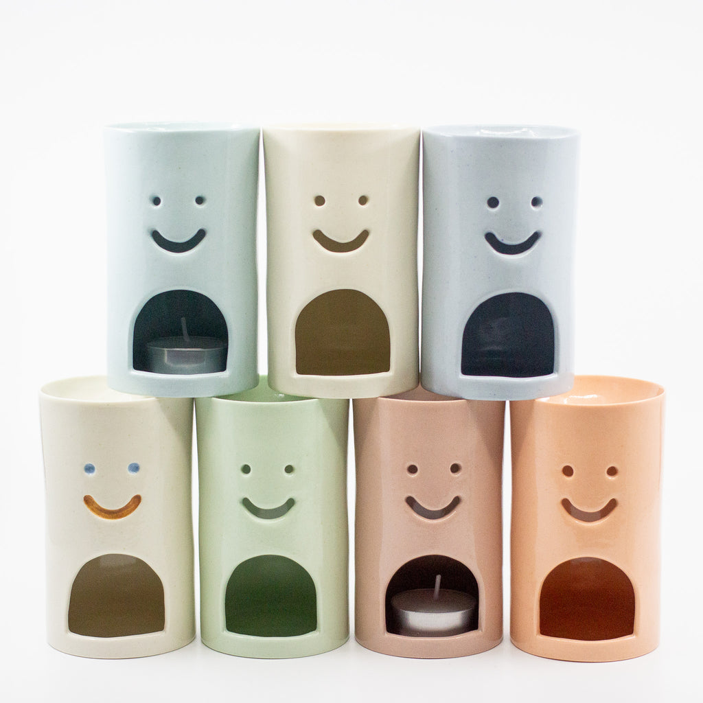 Set of six cylindrical oil burners with smiley face designs on a white background