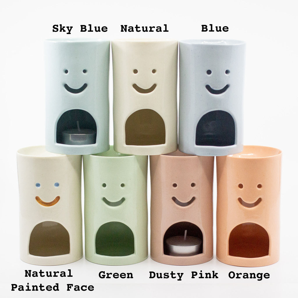 Set of cylindrical oil burners with smiley faces in various colors and finishes.