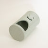 A green ceramic cylindrical container with a smiley face cutout on one end and a large arched opening on the side, photographed on a plain white background.