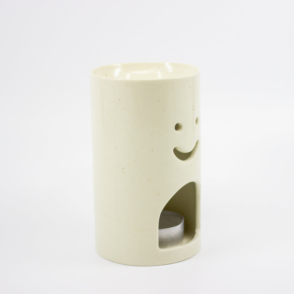 Cylindrical ceramic oil burner with smiley face design on a white background