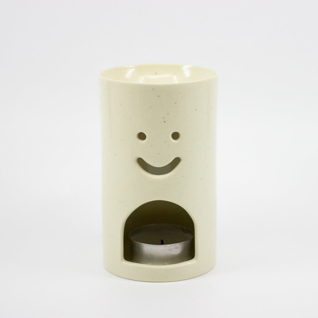Cylindrical ceramic oil burner with a smiley face design on a white background