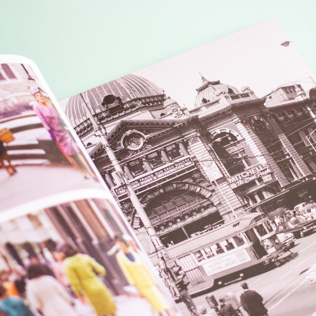 An open printed photo book spread, showing a black-and-white architectural street scene on the right page and colourful cropped photos on the left page, photographed against a pale mint background.