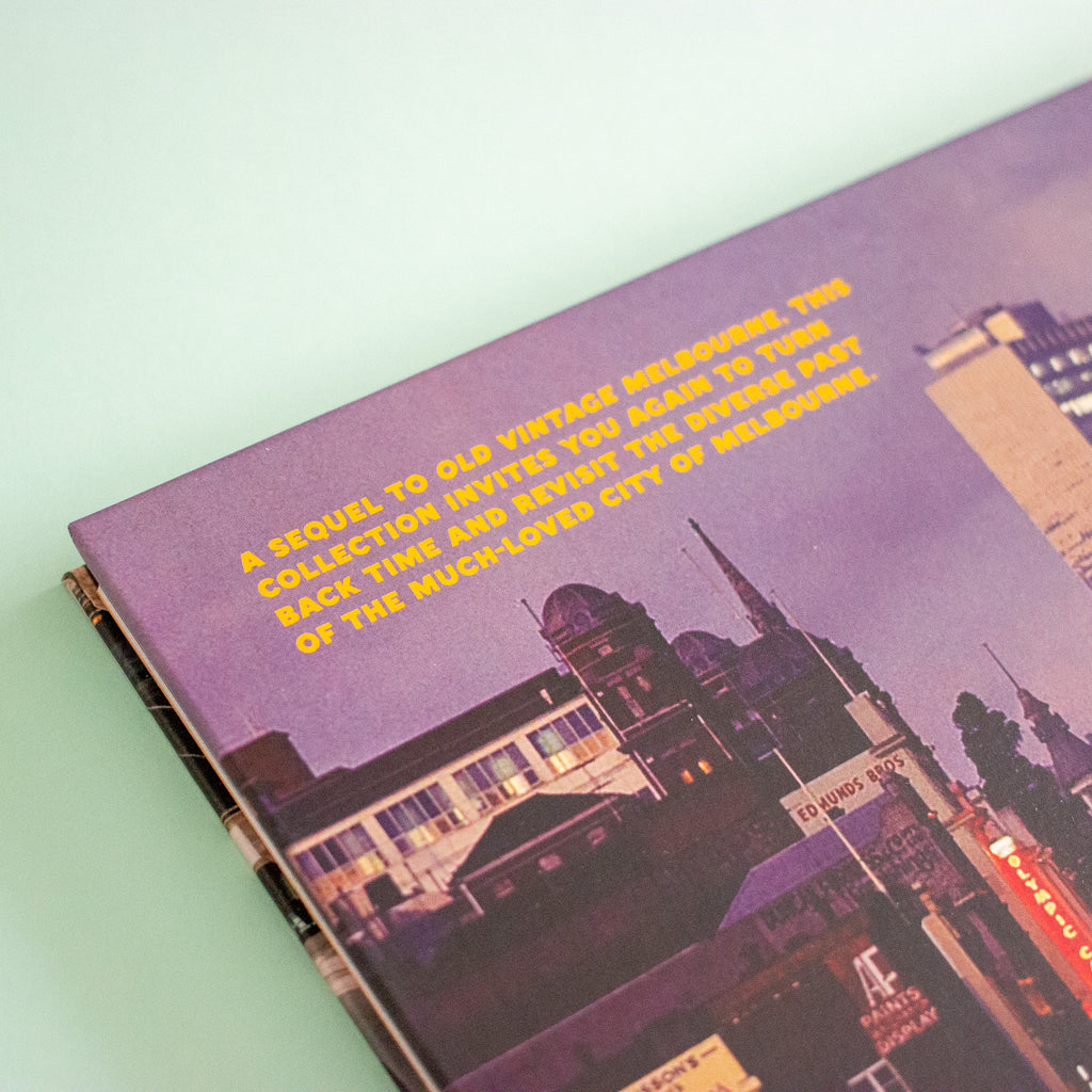 A close-up of a book featuring a vintage-style cityscape in purple tones with bright yellow text, photographed on a pale mint background.
