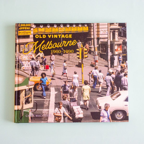 A close-up, angled view of a book, showing a vintage photograph of a city street with tram, traffic lights, and a car. The background around the book is a pale mint green.