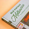 Close-up of a book cover titled "Old Vintage Melbourne" with green lettering on a white background, photographed at an angle against a peach-coloured backdrop.