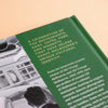 A close-up of a green book cover featuring white text and a black-and-white photograph, photographed on a warm beige background.