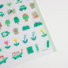 A close-up of a sheet of cute, small cartoon stickers on a white background. The stickers feature playful green and yellow characters, including trees, flowers, a cat in a car, and simple objects, all with smiling faces.