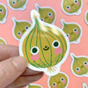 Sticker of a cartoon onion with a face held by a hand against a background of similar magnets.