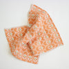 An orange and white patterned cloth with small green floral details, draped on a clean white background.