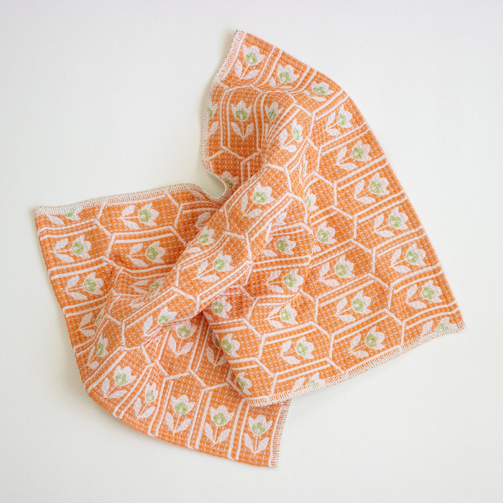 An orange and white patterned cloth with small green floral details, draped on a clean white background.