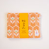 An orange and white patterned cotton towel with a bright orange paper label wrapped around it, photographed on a clean white background. The label features Japanese text and a small KONTEX brand tag.