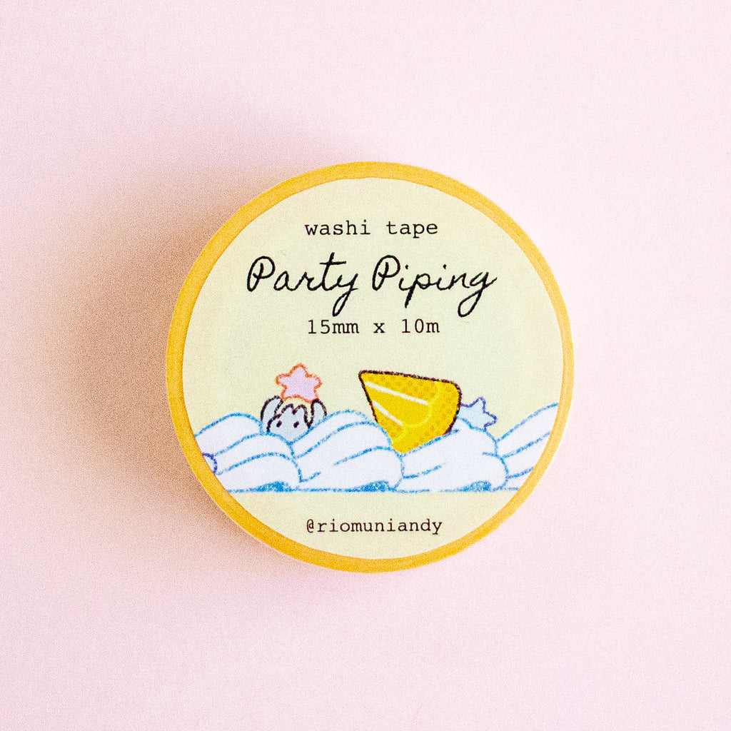 A round roll of washi tape labeled 'Party Piping' by @riomuniandy, featuring a yellow border and a pastel illustration of a yellow cookie and blue waves on a cream background, set against a soft pink backdrop.