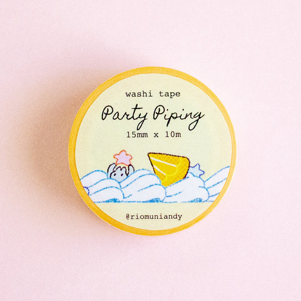 A round roll of washi tape labeled 'Party Piping' by @riomuniandy, featuring a yellow border and a pastel illustration of a yellow cookie and blue waves on a cream background, set against a soft pink backdrop.