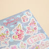 A pastel-themed sticker sheet titled 'Pastel Decora' featuring cute cartoon characters on a light blue polka-dot background, photographed on a warm beige surface.