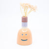 Front view of the persimmon vase with flower. Orange colour, blue smile, multicoloured spout. 