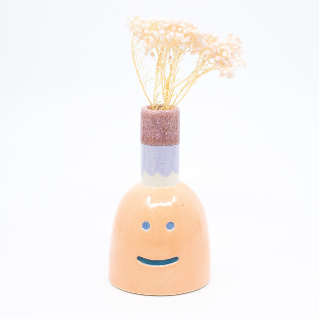 Front view of the persimmon vase with flower. Orange colour, blue smile, multicoloured spout. 