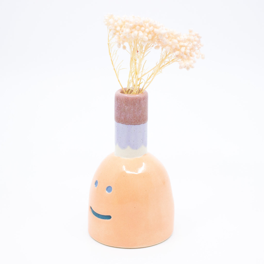 Side view of the persimmon vase with flower. Orange colour, blue smile, multicoloured spout. 