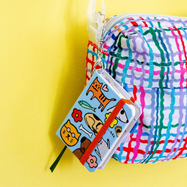 Colourful plaid bag with a small notebook featuring cartoon cat and dog designs on a yellow background