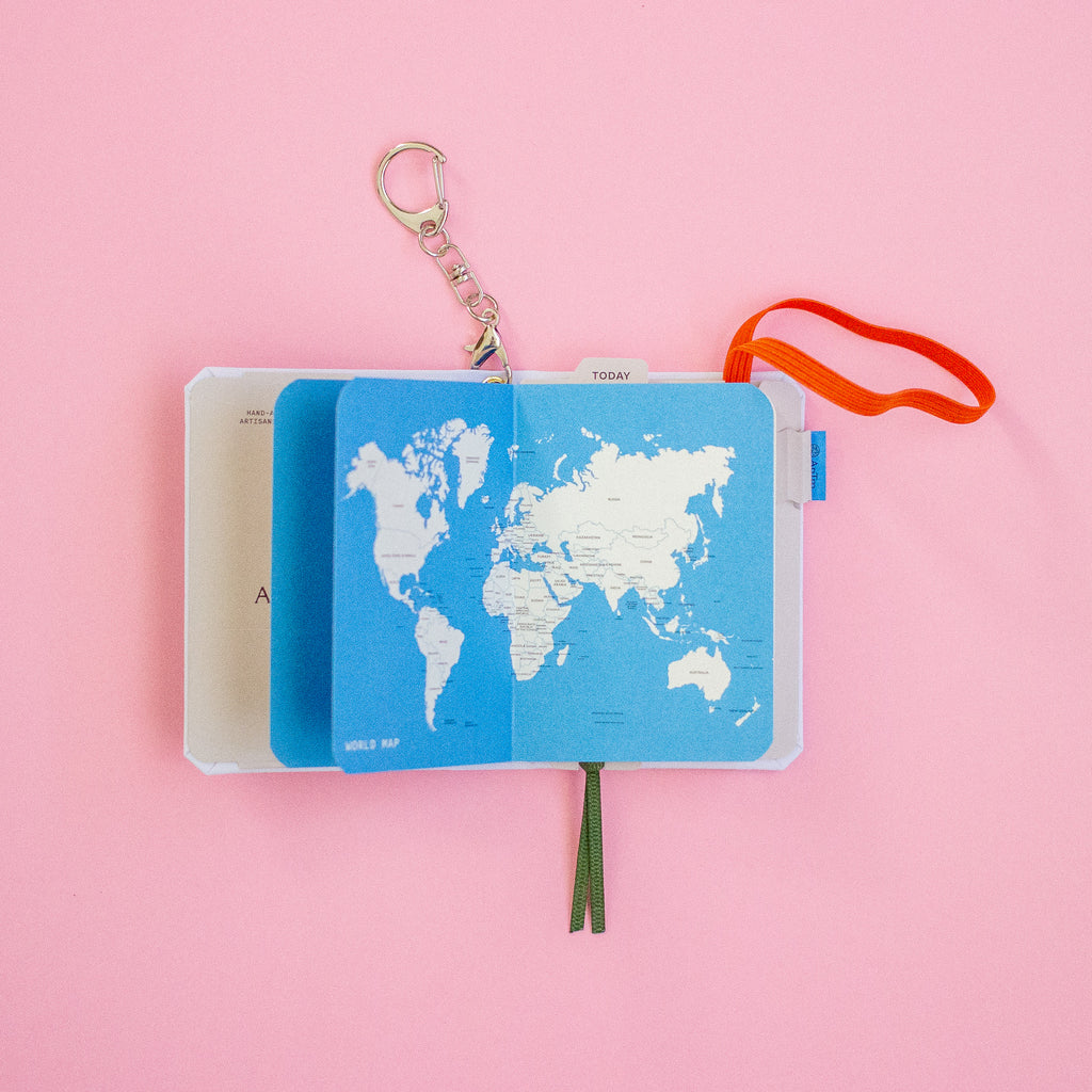 Blue world map notebook with a keychain on a pink background