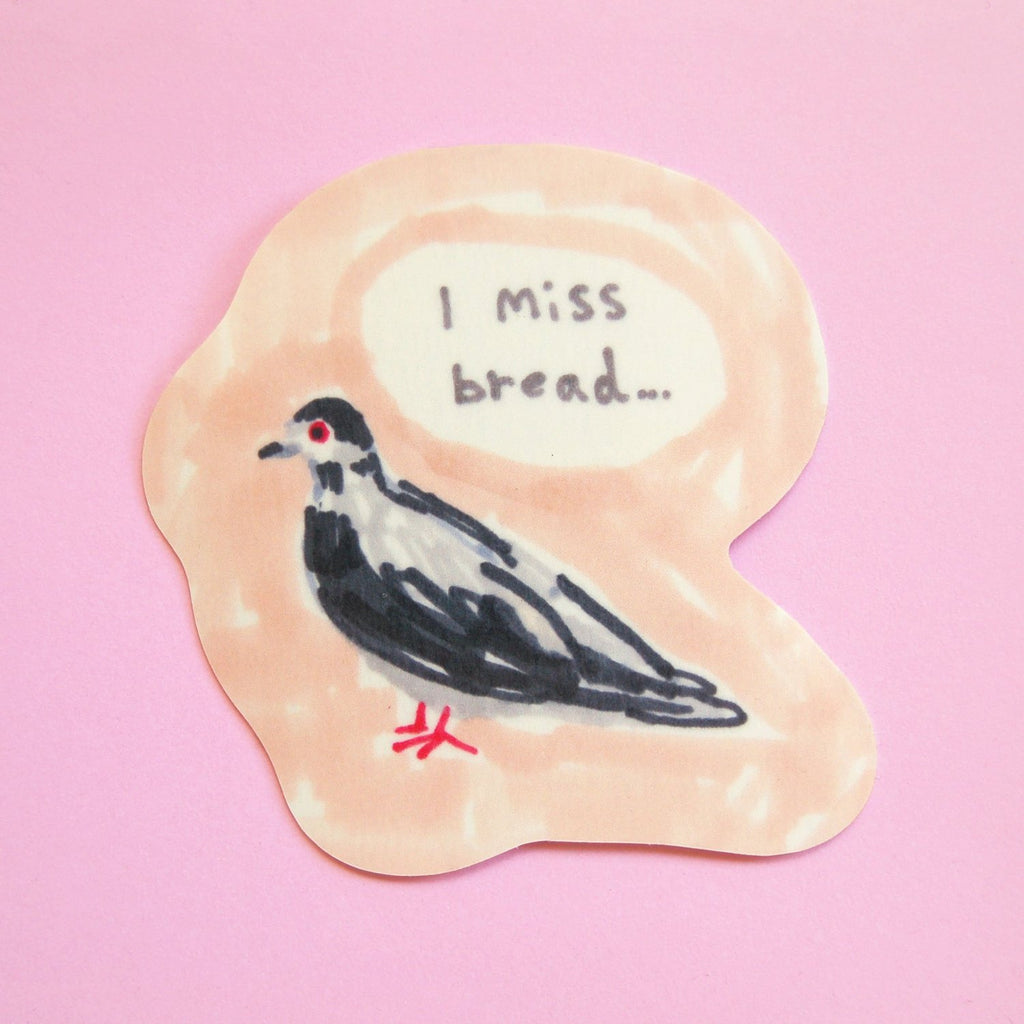 A die-cut sticker featuring a hand-drawn black and white bird with a red eye and red beak, set on a peach-colored background with a speech bubble that reads 'I miss bread.