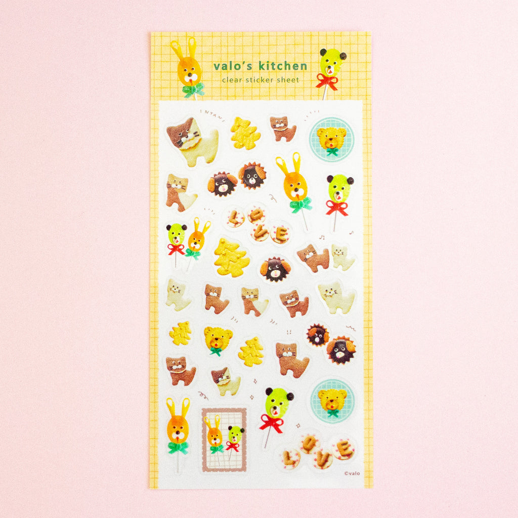 A sheet of cute animal-themed stickers from 'valo's kitchen' featuring teddy bears, bunnies, and dogs in yellow, brown, and green, displayed on a soft pink background.
