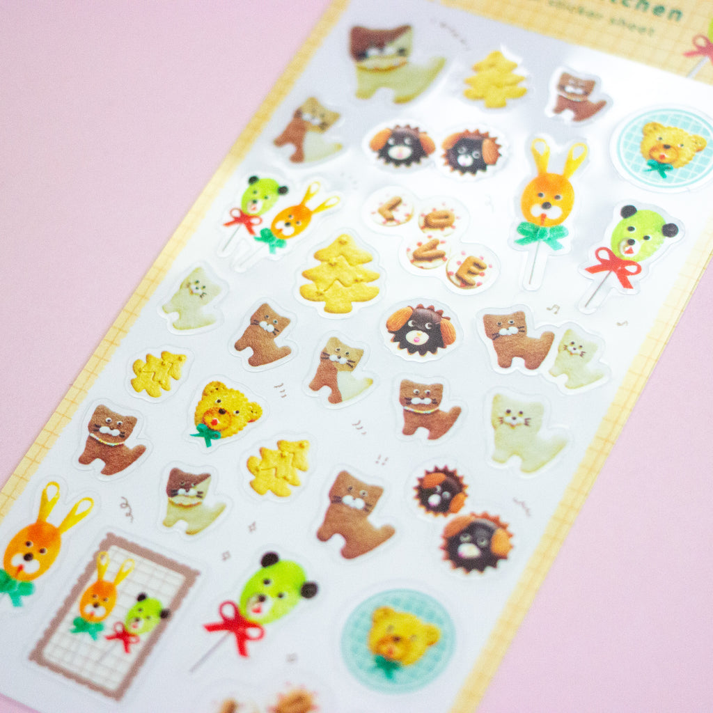 A sheet of cute cartoon animal stickers laid diagonally on a pink background. The stickers feature various characters in brown, yellow, green, and beige tones, including bears, rabbits, cats, and small decorative motifs.